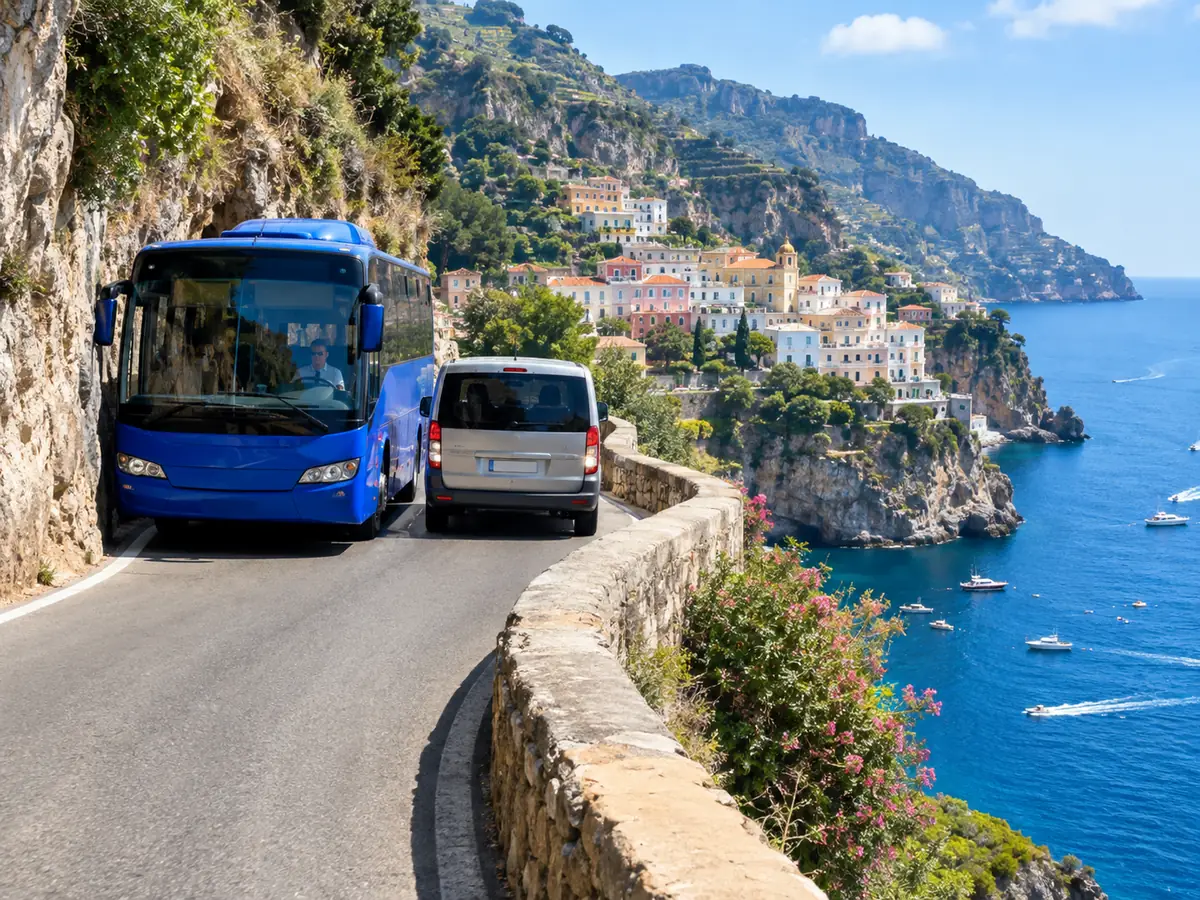 Ein blauer Bus und ein Minivan begegnen sich auf einer schmalen Klippenstraße über dem Meer